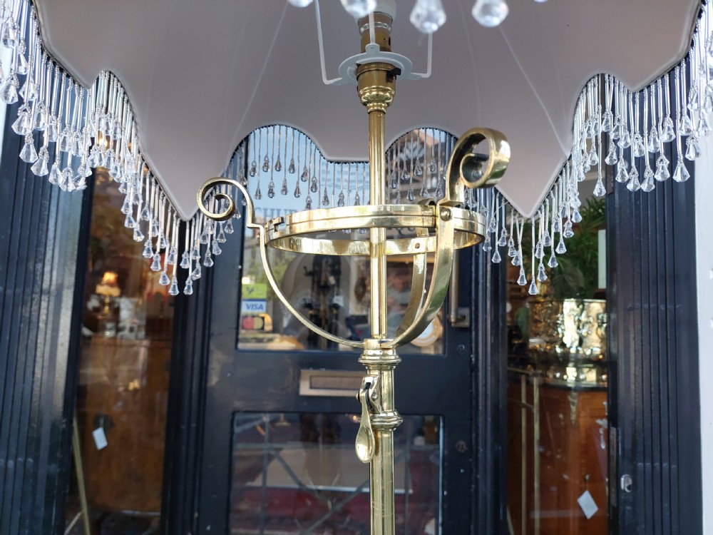 An Arts and Crafts brass standard floor lamp featuring a scrollwork tripod base, floral copper accents, and a fringe-trimmed domed shade. View IV