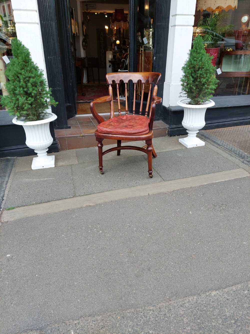An early 19th-century mahogany desk chair featuring a spindle back, curved armrests, a red leather seat cushion, turned front legs, and brass castors. View II