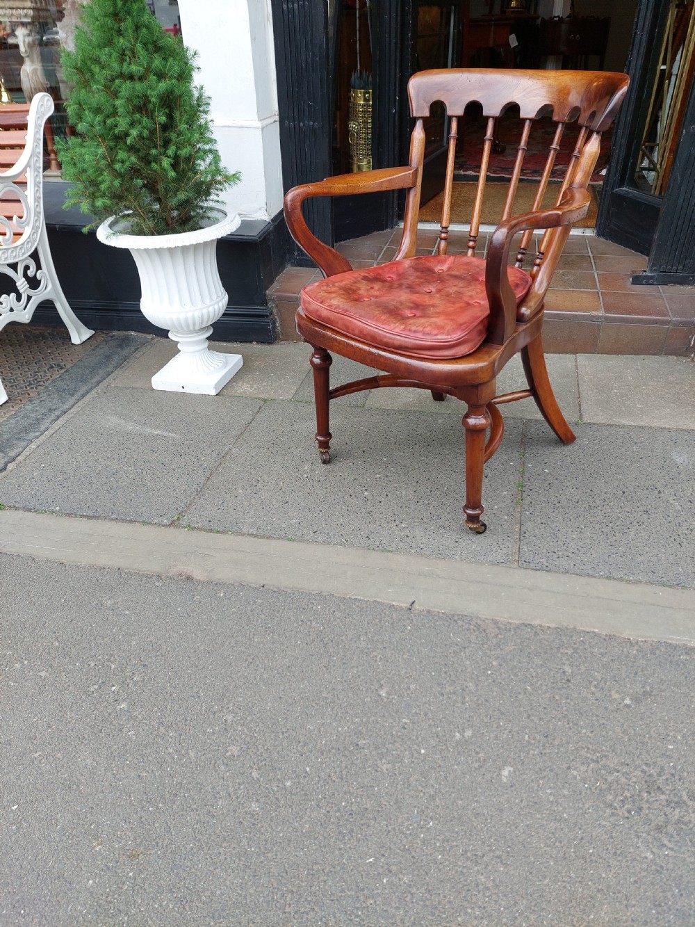 An early 19th-century mahogany desk chair featuring a spindle back, curved armrests, a red leather seat cushion, turned front legs, and brass castors. View III
