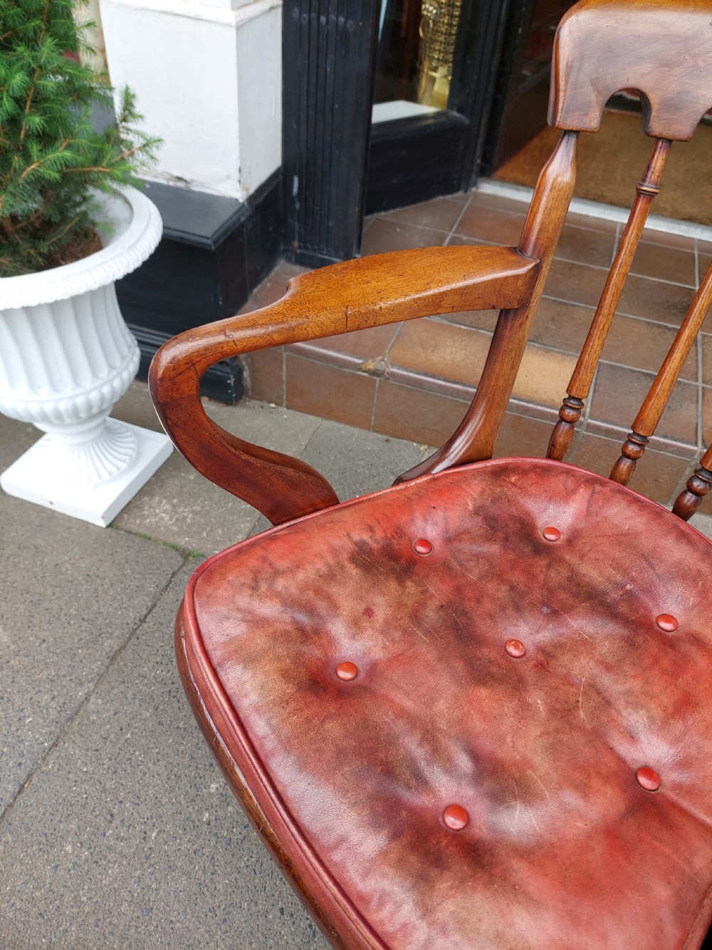 An early 19th-century mahogany desk chair featuring a spindle back, curved armrests, a red leather seat cushion, turned front legs, and brass castors. View VI