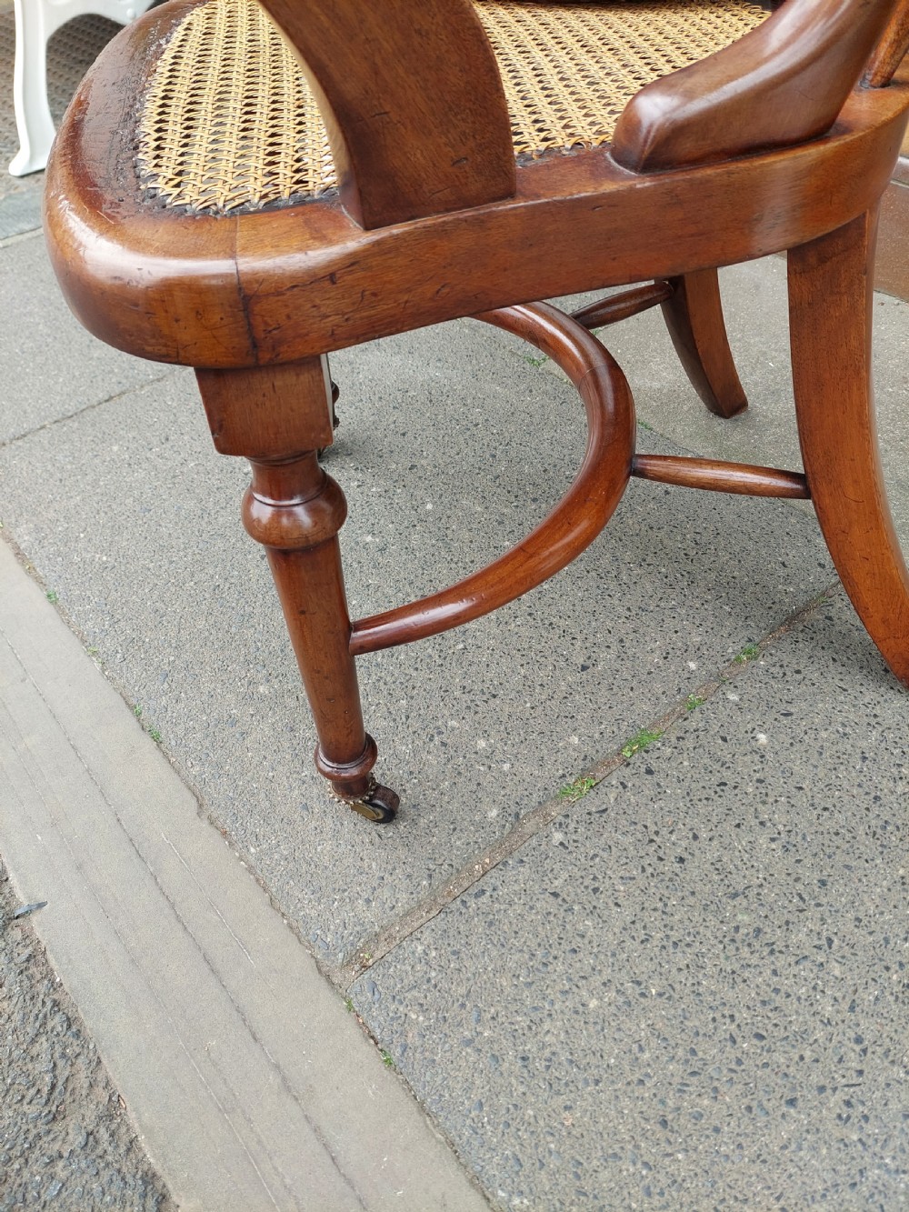 An early 19th-century mahogany desk chair featuring a spindle back, curved armrests, a red leather seat cushion, turned front legs, and brass castors. View VIII
