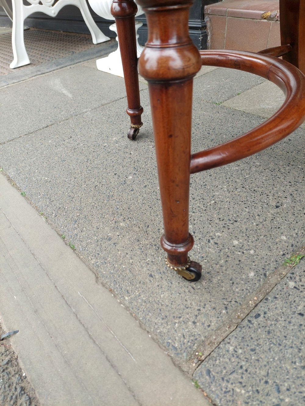 An early 19th-century mahogany desk chair featuring a spindle back, curved armrests, a red leather seat cushion, turned front legs, and brass castors. View IX