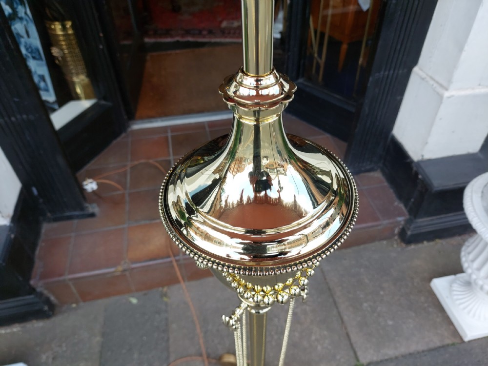 A late nineteenth-century brass standard floor lamp featuring a polished metal column with decorative swags and an ornate pink fabric shade with tassel fringe. View IV