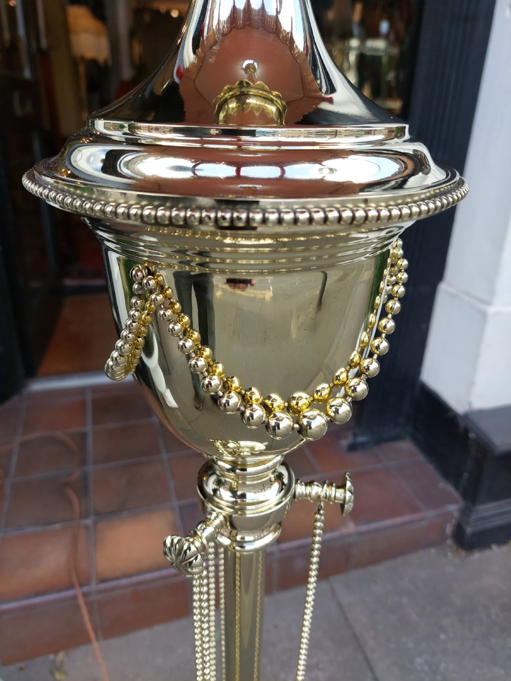 A late nineteenth-century brass standard floor lamp featuring a polished metal column with decorative swags and an ornate pink fabric shade with tassel fringe. View IX