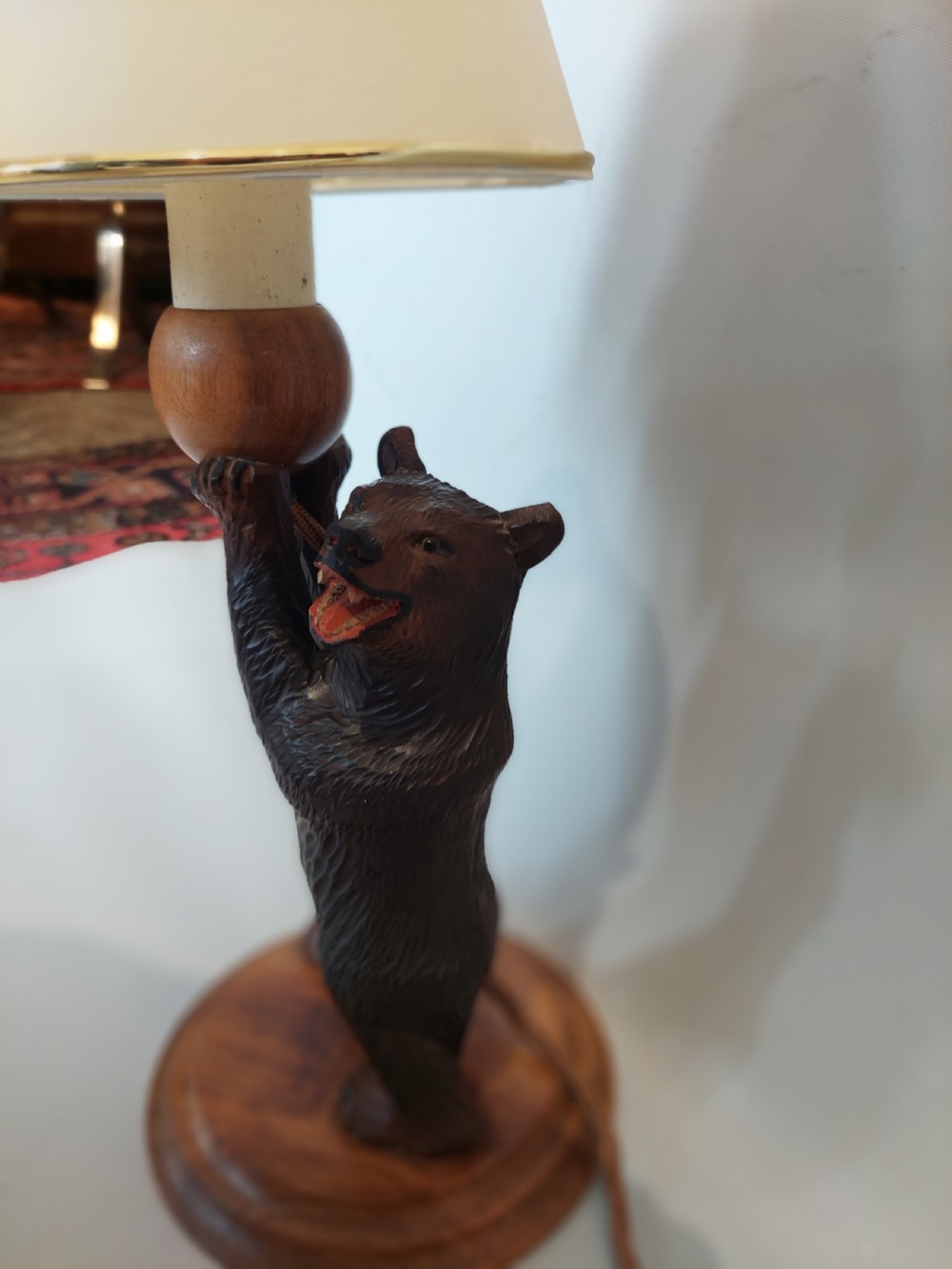 A dark hand-carved wooden bear standing on a turned base holding up a conical cream lampshade. View IV
