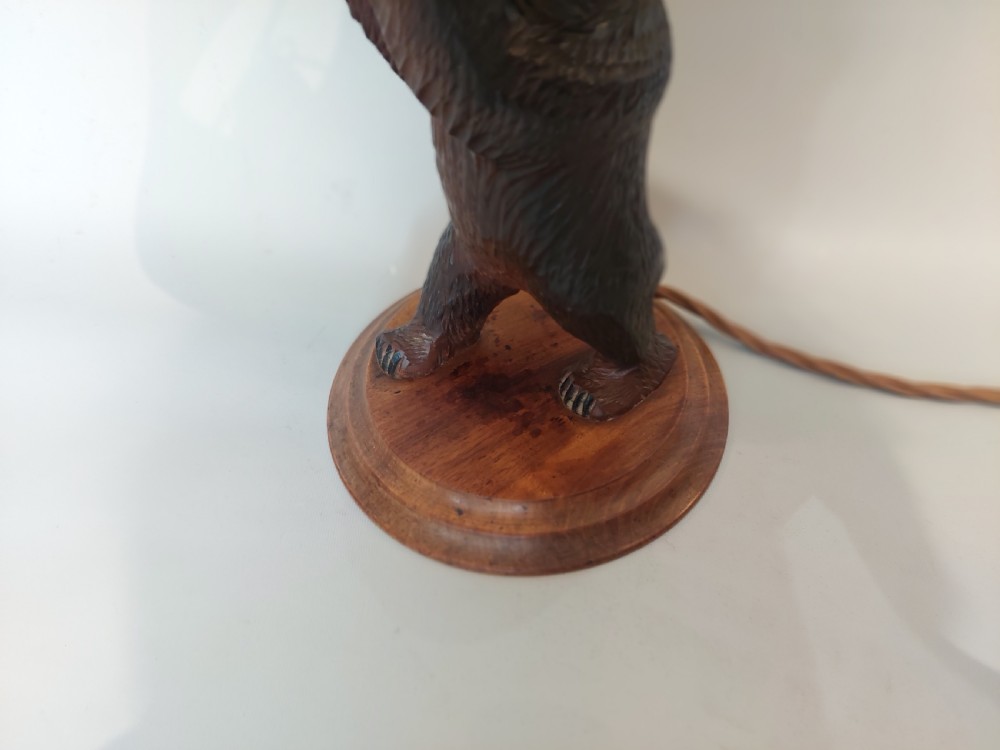 A dark hand-carved wooden bear standing on a turned base holding up a conical cream lampshade. View V