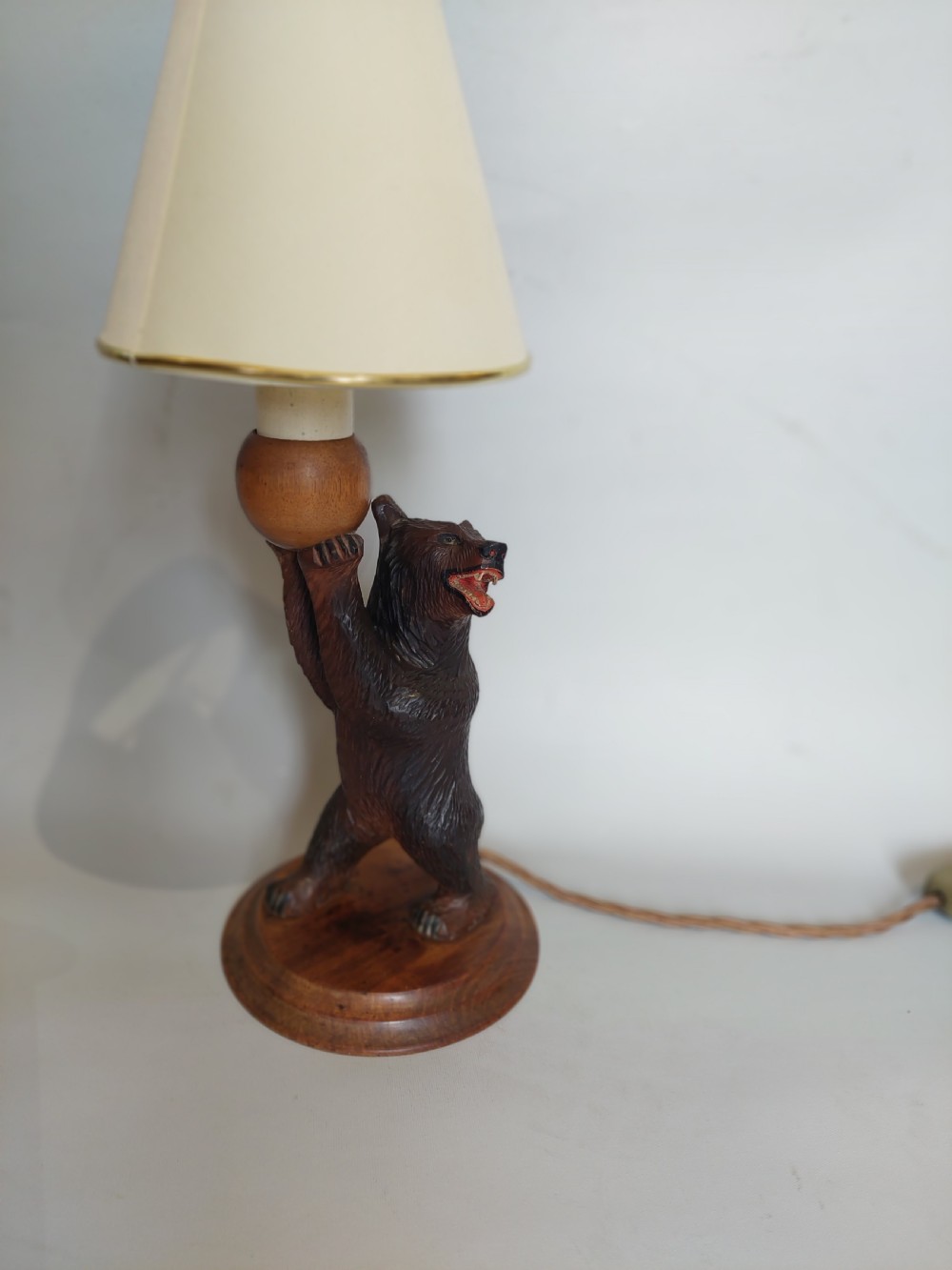 A dark hand-carved wooden bear standing on a turned base holding up a conical cream lampshade. View VI