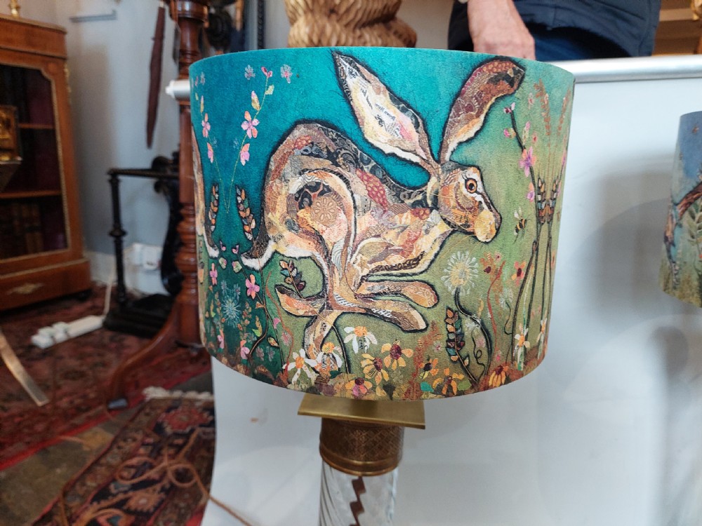A pair of early 20th-century table lamps with square brass bases, twisted clear glass columns, and drum lampshades featuring countryside wildlife illustrations. View VII