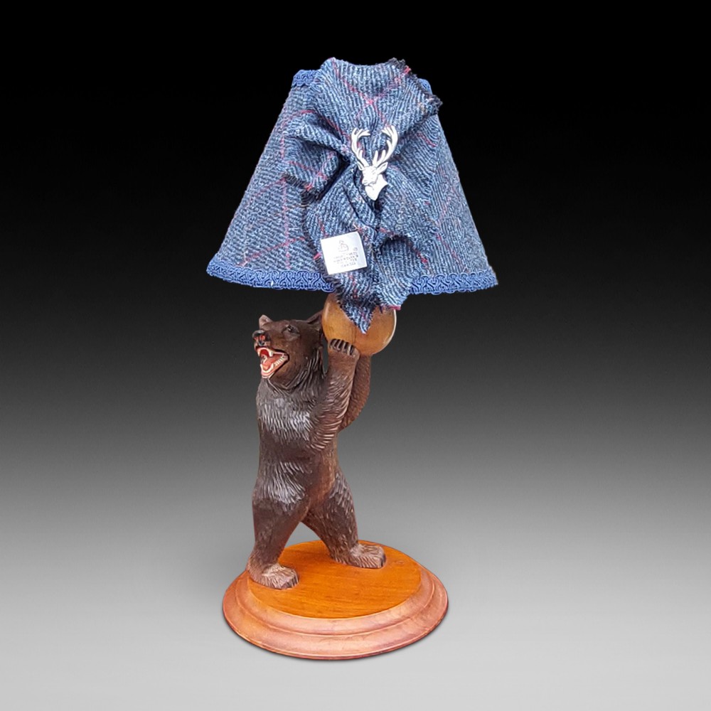 An early twentieth-century carved lindenwood Black Forest bear table lamp topped with a blue tartan fabric lampshade.