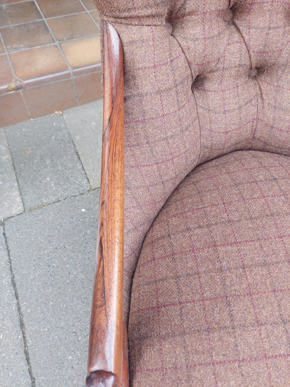 An early 19th-century rosewood armchair with brown button-back upholstery, carved scroll arms, turned front legs, and brass castors. View V