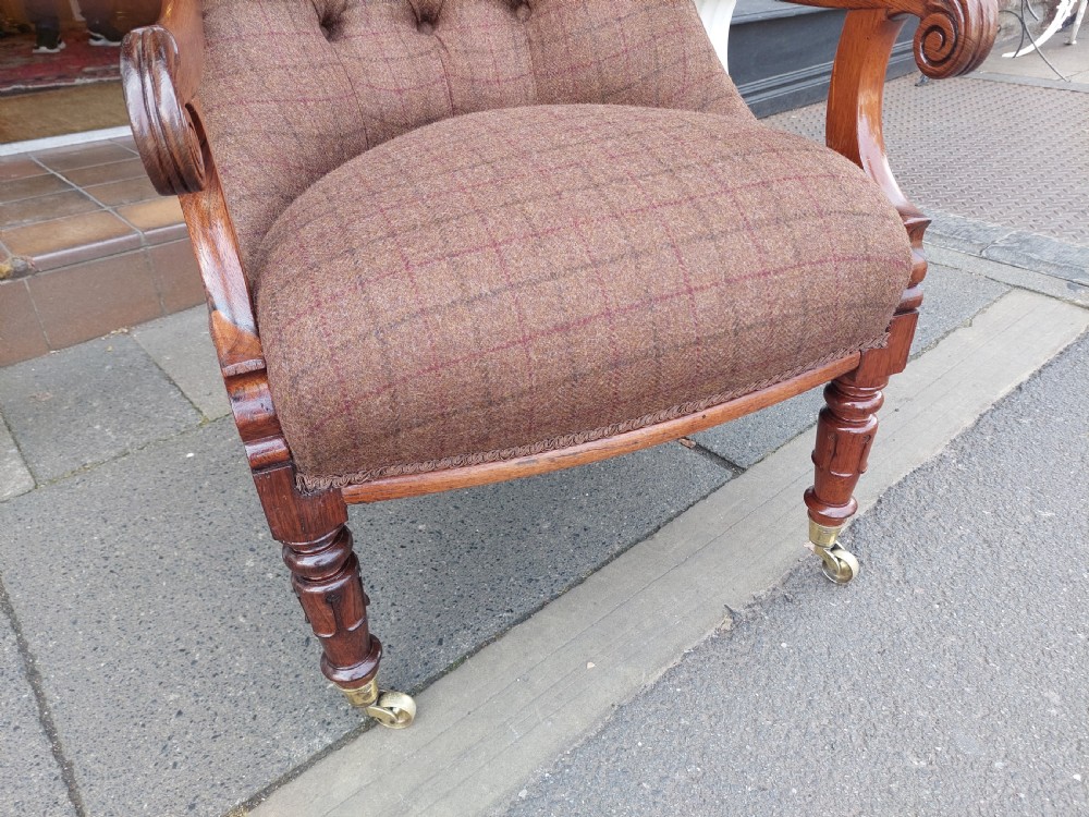 An early 19th-century rosewood armchair with brown button-back upholstery, carved scroll arms, turned front legs, and brass castors. View VI