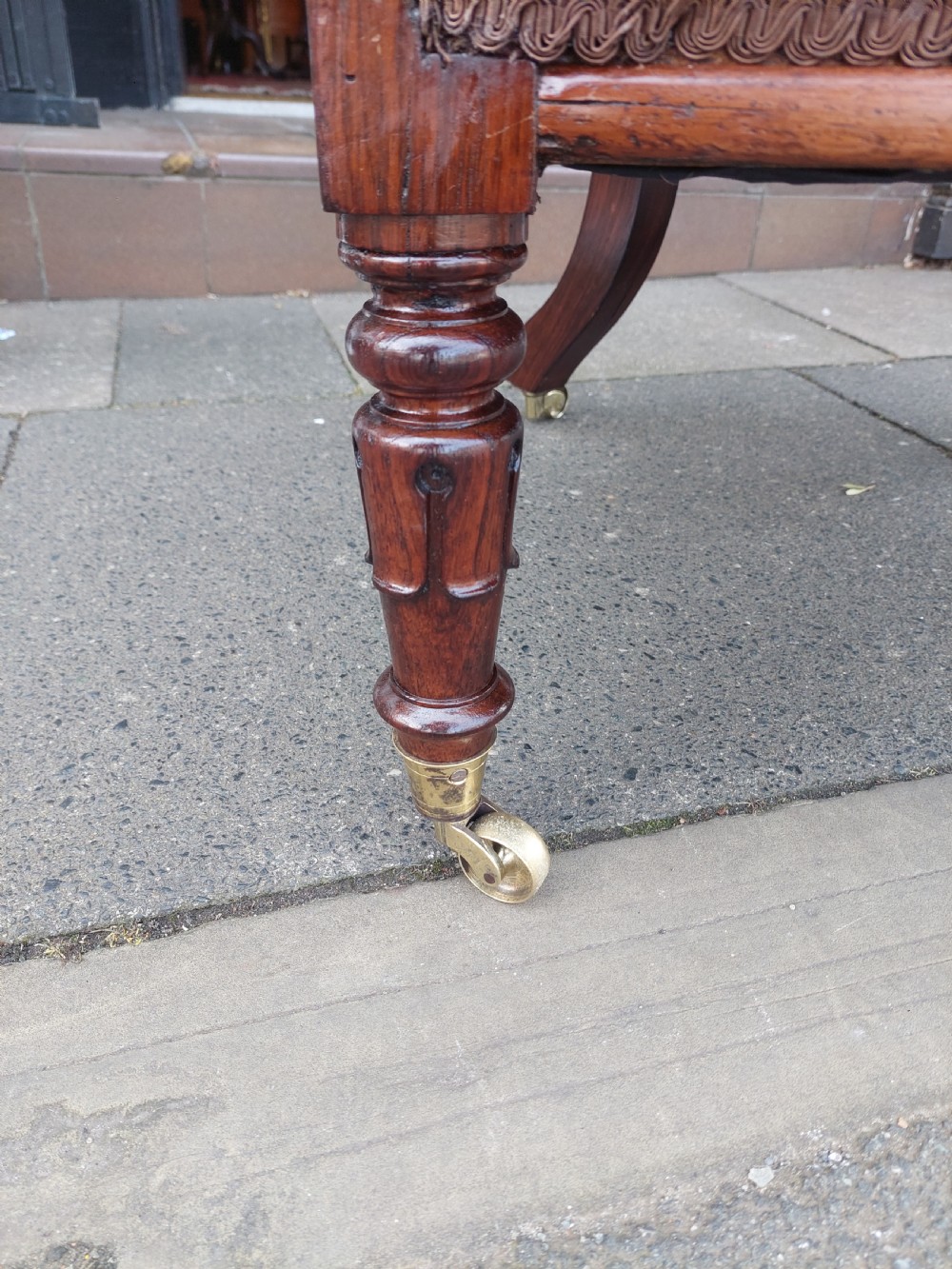 An early 19th-century rosewood armchair with brown button-back upholstery, carved scroll arms, turned front legs, and brass castors. View VII