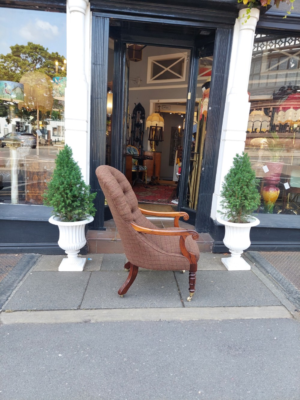 An early 19th-century rosewood armchair with brown button-back upholstery, carved scroll arms, turned front legs, and brass castors. View X