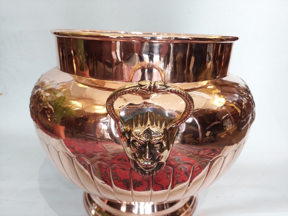 A bulbous Victorian polished copper vessel featuring embossed floral scrollwork, lower gadrooned fluting, two side loop handles, and a circular stepped pedestal base. View IV