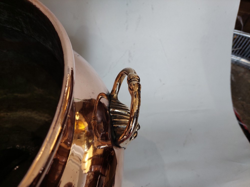A bulbous Victorian polished copper vessel featuring embossed floral scrollwork, lower gadrooned fluting, two side loop handles, and a circular stepped pedestal base. View VI