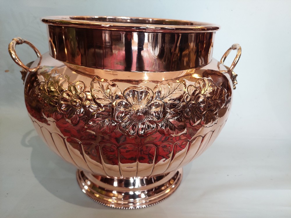 A bulbous Victorian polished copper vessel featuring embossed floral scrollwork, lower gadrooned fluting, two side loop handles, and a circular stepped pedestal base. View VII