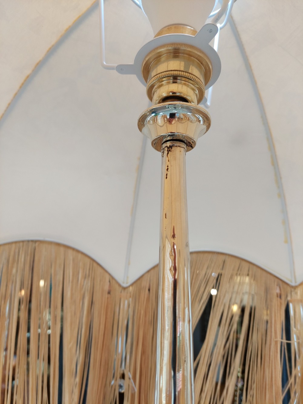 A tall floor lamp made from a tapered copper and white metal horn stem topped with a cream fabric dome shade featuring long tassel fringe. View VII