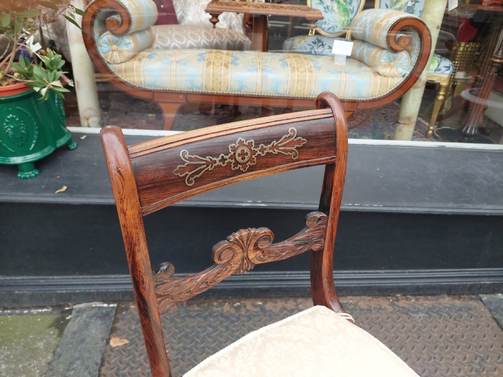 A set of six English Regency dining chairs featuring faux rosewood graining, brass inlay on the top rails, carved central splats, sabre front legs, and cream upholstered cushions. View III