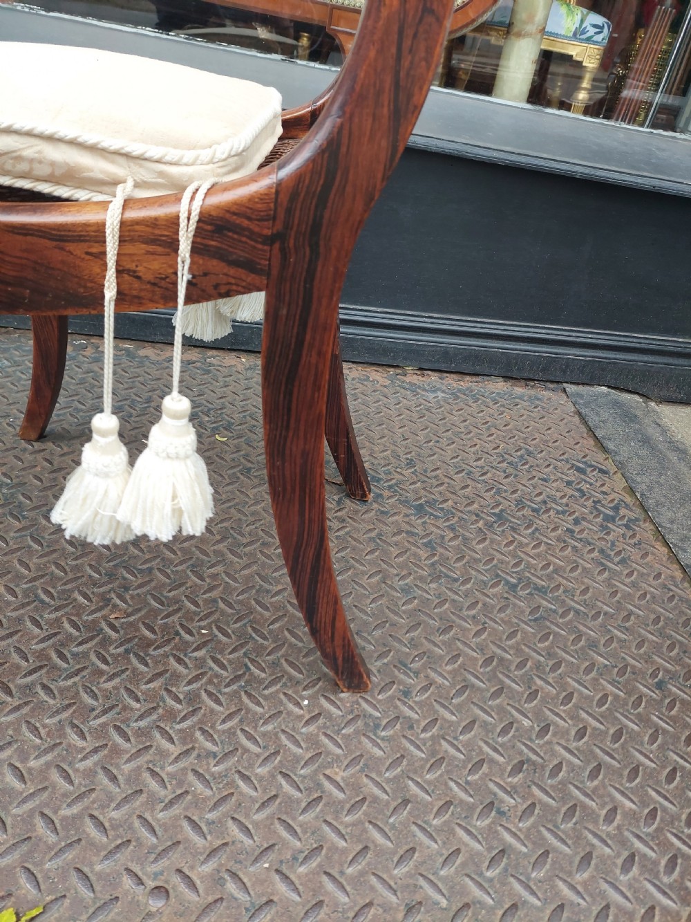 A set of six English Regency dining chairs featuring faux rosewood graining, brass inlay on the top rails, carved central splats, sabre front legs, and cream upholstered cushions. View VI
