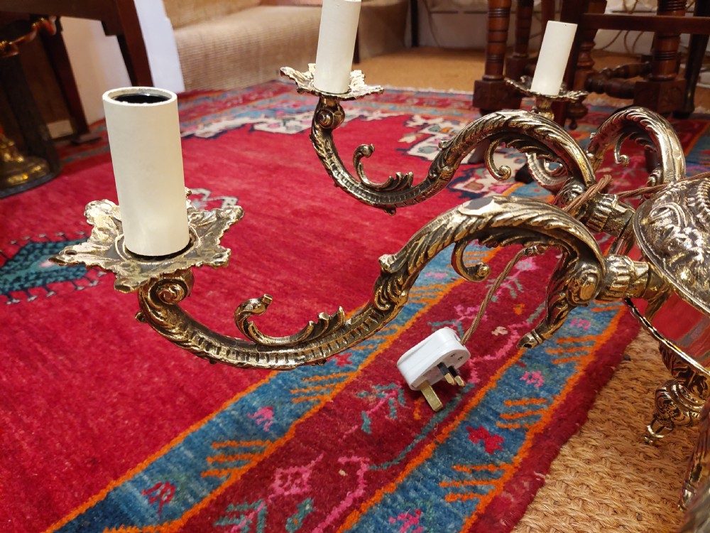 An eight-arm cast brass chandelier featuring detailed acanthus leaf mounts, scrollwork arms, and white candle-effect lamp holders. View II