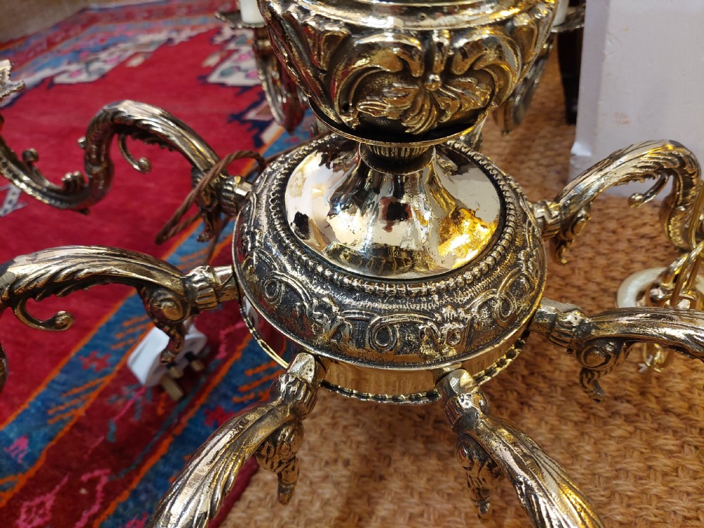 An eight-arm cast brass chandelier featuring detailed acanthus leaf mounts, scrollwork arms, and white candle-effect lamp holders. View V