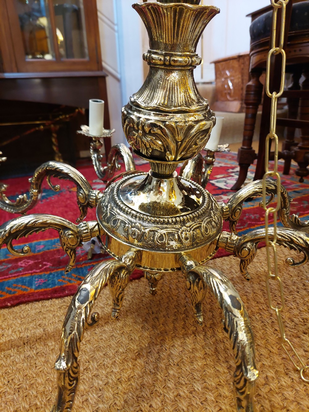 An eight-arm cast brass chandelier featuring detailed acanthus leaf mounts, scrollwork arms, and white candle-effect lamp holders. View VI