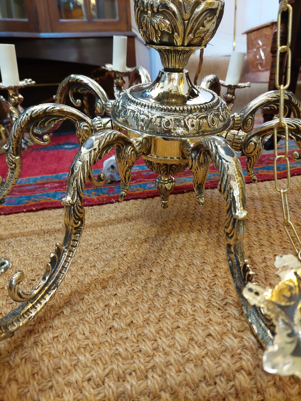 An eight-arm cast brass chandelier featuring detailed acanthus leaf mounts, scrollwork arms, and white candle-effect lamp holders. View VII
