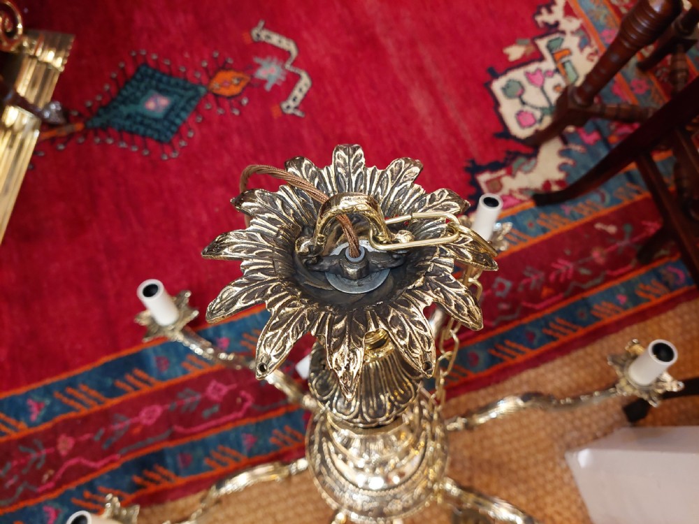 An eight-arm cast brass chandelier featuring detailed acanthus leaf mounts, scrollwork arms, and white candle-effect lamp holders. View XII