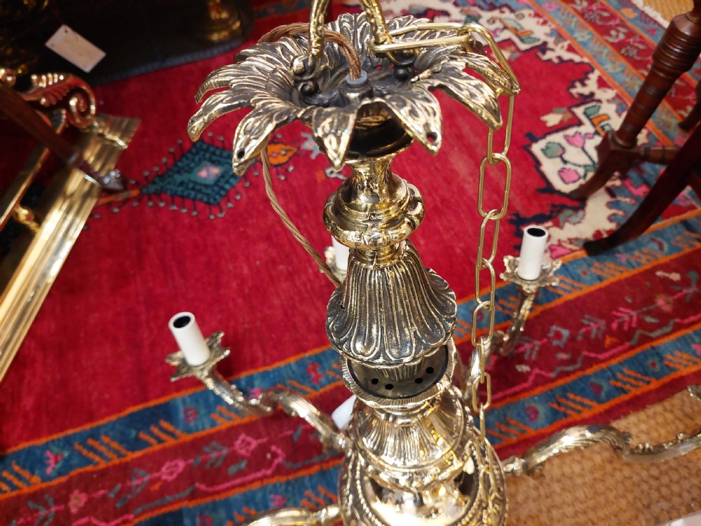 An eight-arm cast brass chandelier featuring detailed acanthus leaf mounts, scrollwork arms, and white candle-effect lamp holders. View XIII