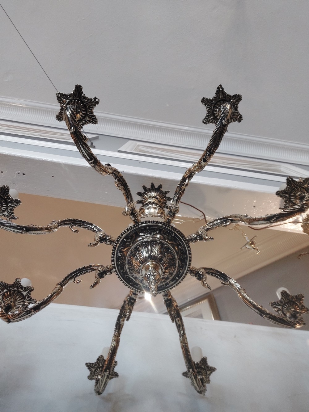 An eight-arm cast brass chandelier featuring detailed acanthus leaf mounts, scrollwork arms, and white candle-effect lamp holders. View XVI