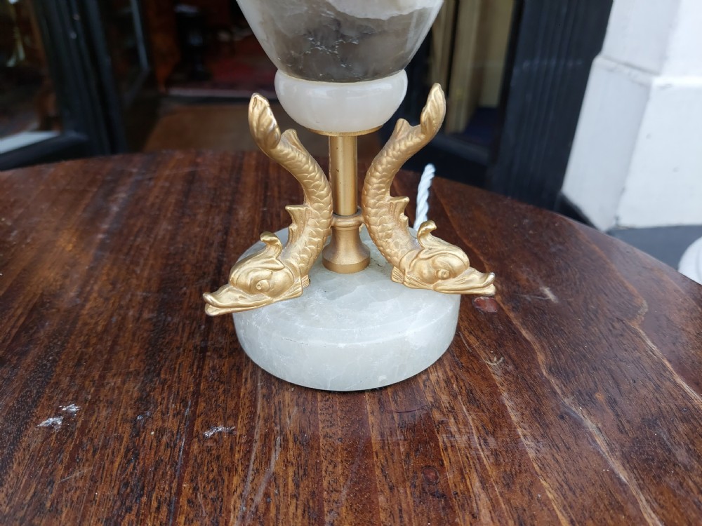 A pair of white veined onyx table lamps featuring gilt metal dolphin feet and flared white fabric shades with fringe. View II