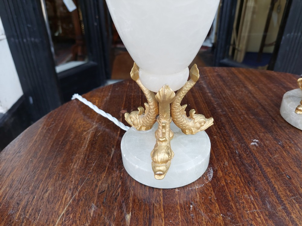 A pair of white veined onyx table lamps featuring gilt metal dolphin feet and flared white fabric shades with fringe. View III