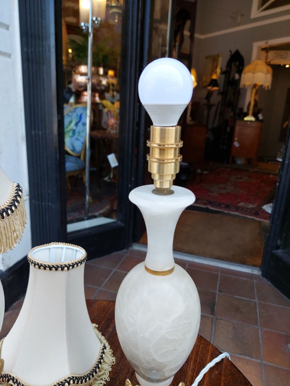 A pair of white veined onyx table lamps featuring gilt metal dolphin feet and flared white fabric shades with fringe. View V