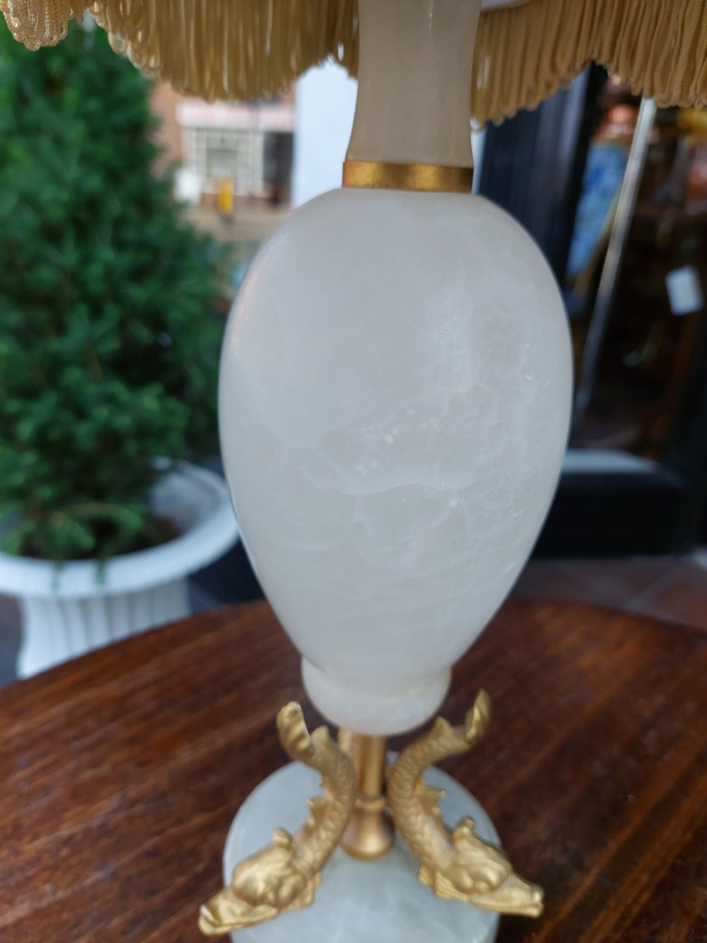 A pair of white veined onyx table lamps featuring gilt metal dolphin feet and flared white fabric shades with fringe. View VI