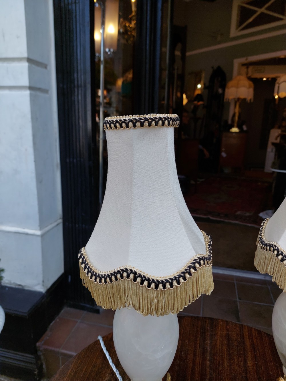 A pair of white veined onyx table lamps featuring gilt metal dolphin feet and flared white fabric shades with fringe. View VII