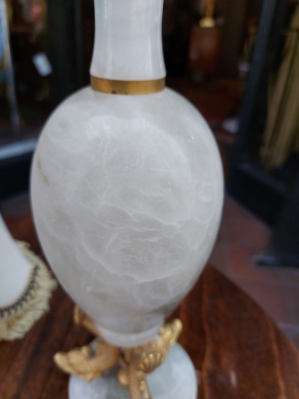 A pair of white veined onyx table lamps featuring gilt metal dolphin feet and flared white fabric shades with fringe. View VIII