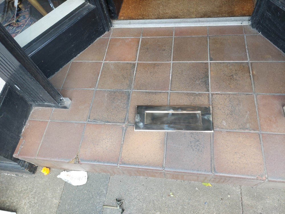 A rectangular polished metal letter box cover plate featuring a central hinged flap and a smooth outer frame. View II