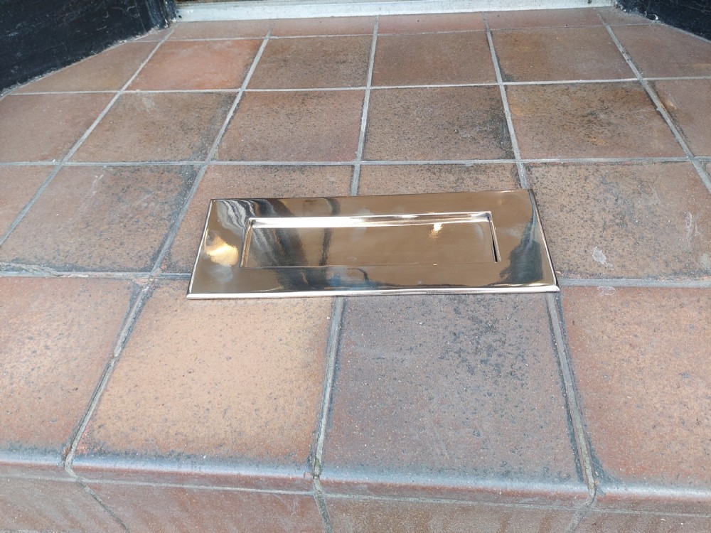 A rectangular polished metal letter box cover plate featuring a central hinged flap and a smooth outer frame. View III