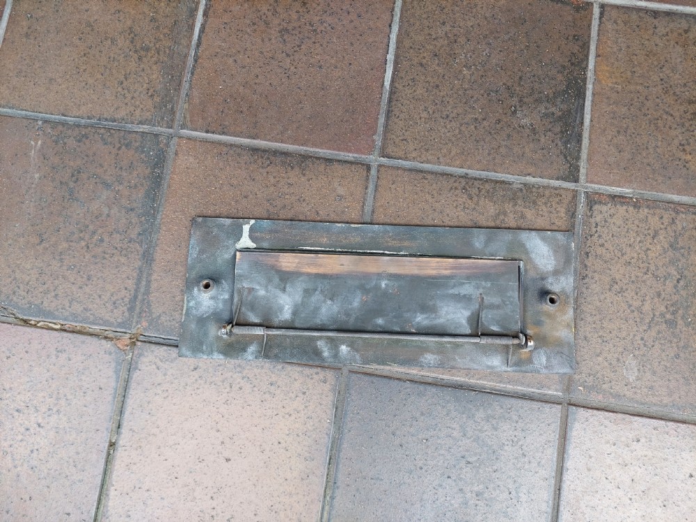A rectangular polished metal letter box cover plate featuring a central hinged flap and a smooth outer frame. View IV