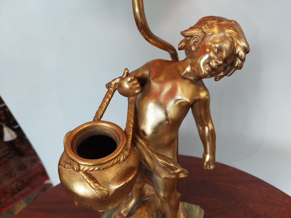A 19th-century French gilt bronze table lamp featuring a sculpted cherub carrying a vessel, mounted on a marble plinth and topped with a red fringed dome shade. View VI
