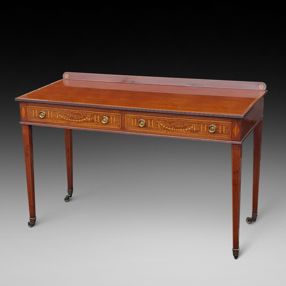 An Edwardian mahogany hall table featuring two inlaid drawers with brass ring handles, tapered square legs with brass castors, and a low rear gallery.