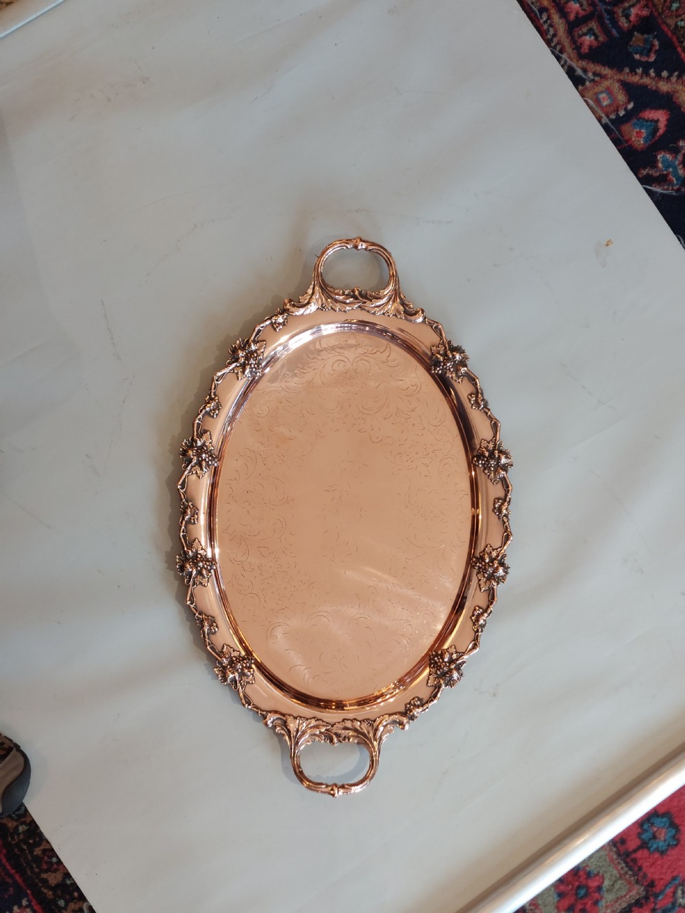 A 19th-century oval copper serving tray featuring detailed scrollwork engraving on the surface, a relief grapevine border, and two cast handles. View II