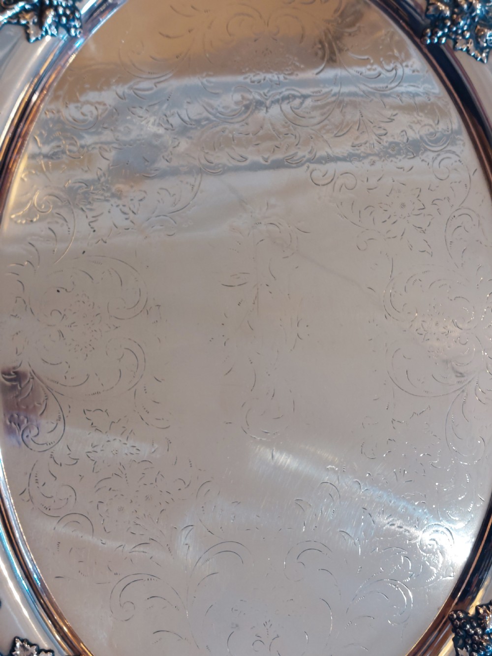A 19th-century oval copper serving tray featuring detailed scrollwork engraving on the surface, a relief grapevine border, and two cast handles. View V