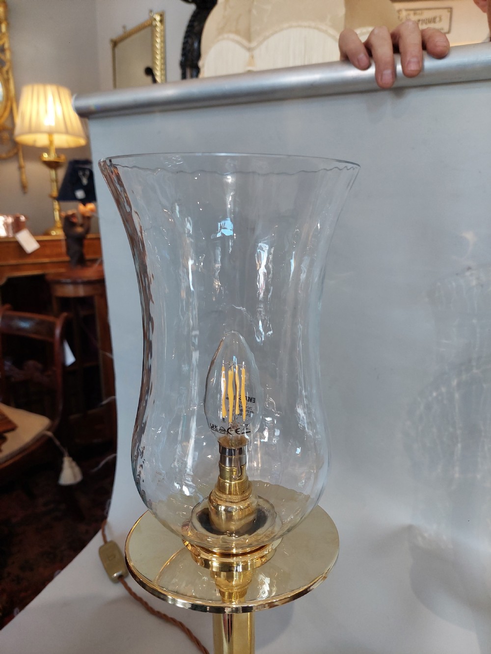 A pair of turned brass table lamps with stepped circular bases, cylindrical stems, and clear flared glass storm shades. View II