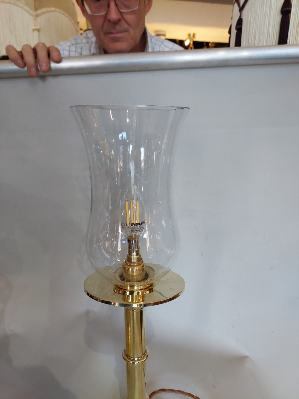 A pair of turned brass table lamps with stepped circular bases, cylindrical stems, and clear flared glass storm shades. View III