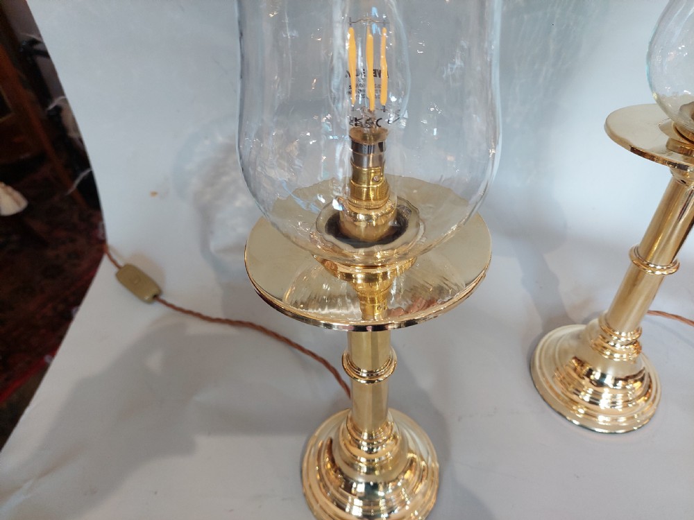 A pair of turned brass table lamps with stepped circular bases, cylindrical stems, and clear flared glass storm shades. View IV