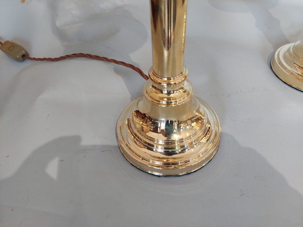 A pair of turned brass table lamps with stepped circular bases, cylindrical stems, and clear flared glass storm shades. View V