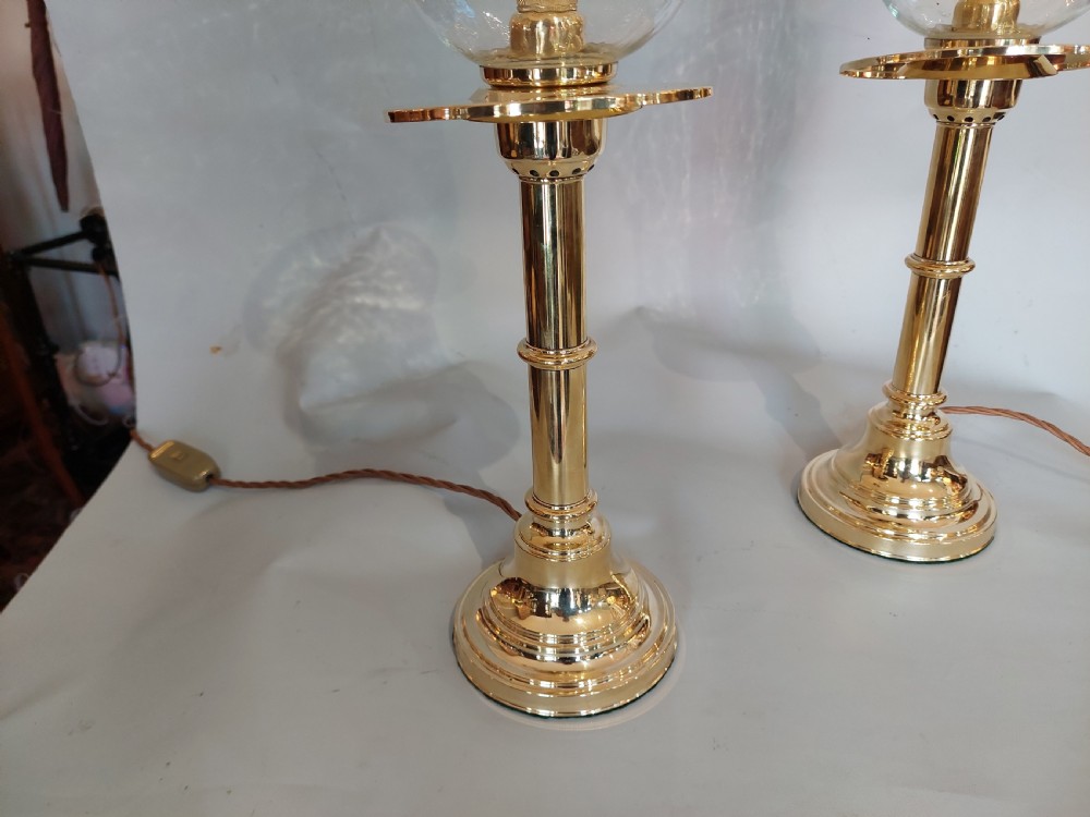 A pair of turned brass table lamps with stepped circular bases, cylindrical stems, and clear flared glass storm shades. View VII