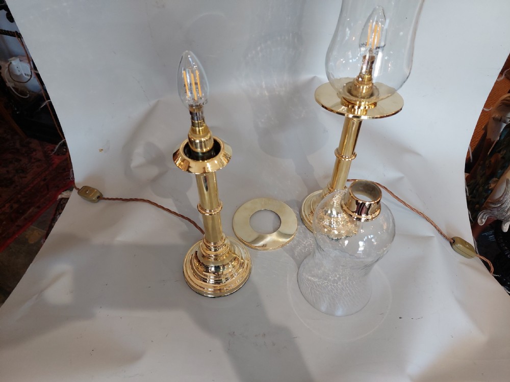 A pair of turned brass table lamps with stepped circular bases, cylindrical stems, and clear flared glass storm shades. View VIII