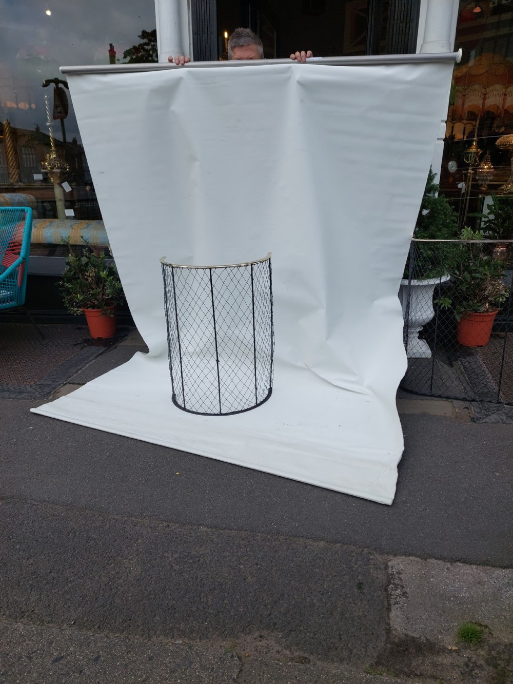 A tall, curved Victorian nursery fender constructed from black wire mesh with vertical iron supports and a polished brass top rail. View II